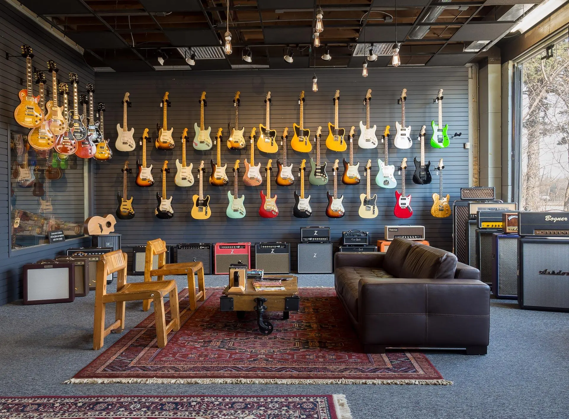 Wall of electric guitars and amplifiers in a premium guitar retail showroom with a seating area