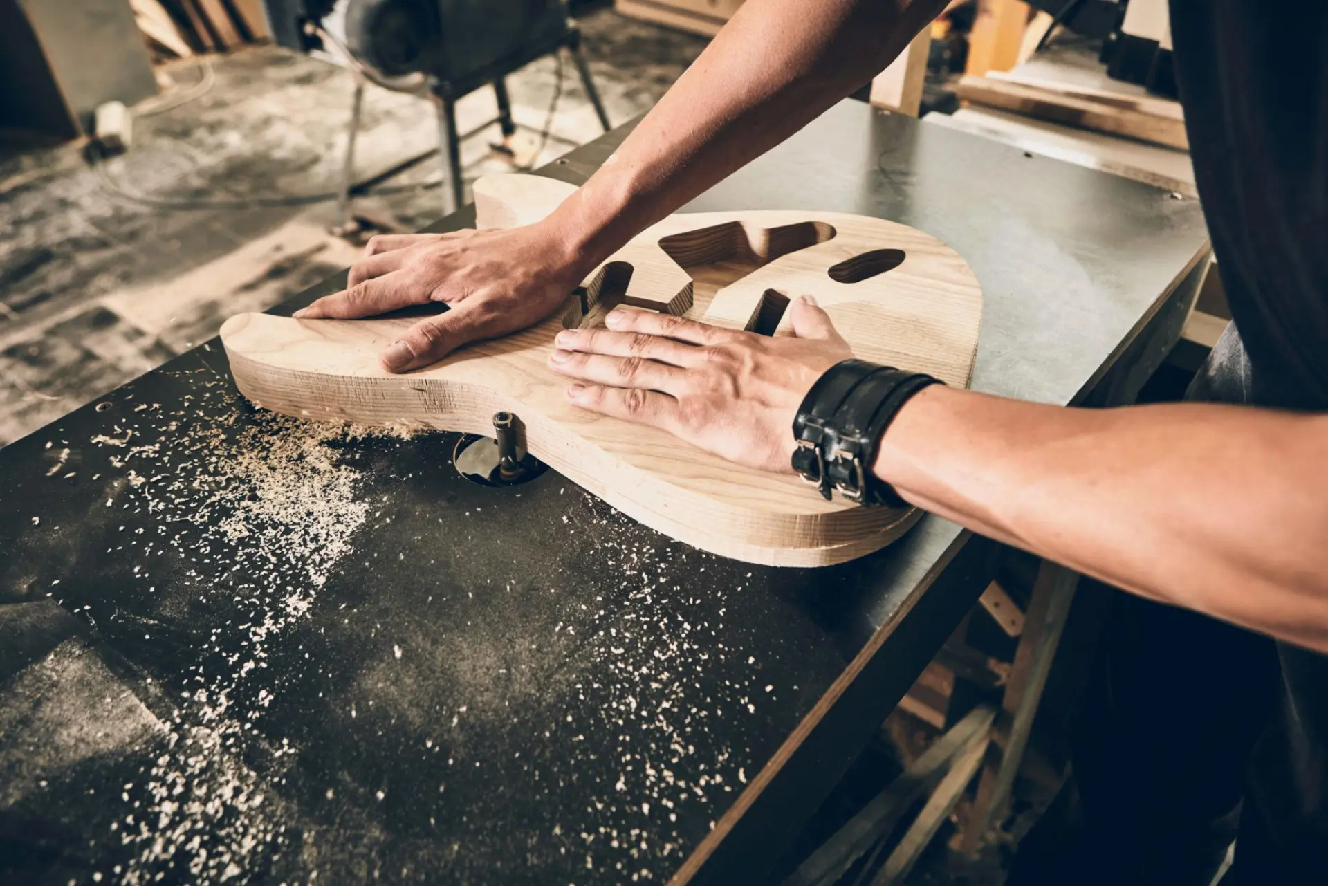 Luthier's hands routing an unfinished wooden guitar body on a workshop bench